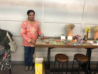 Artists Susan Diane MItchell displays her art on a long table covered in burlap. Her genre is cardboard and found material art. Her works include portraits in series using cardboard, tissue paper and modge podge